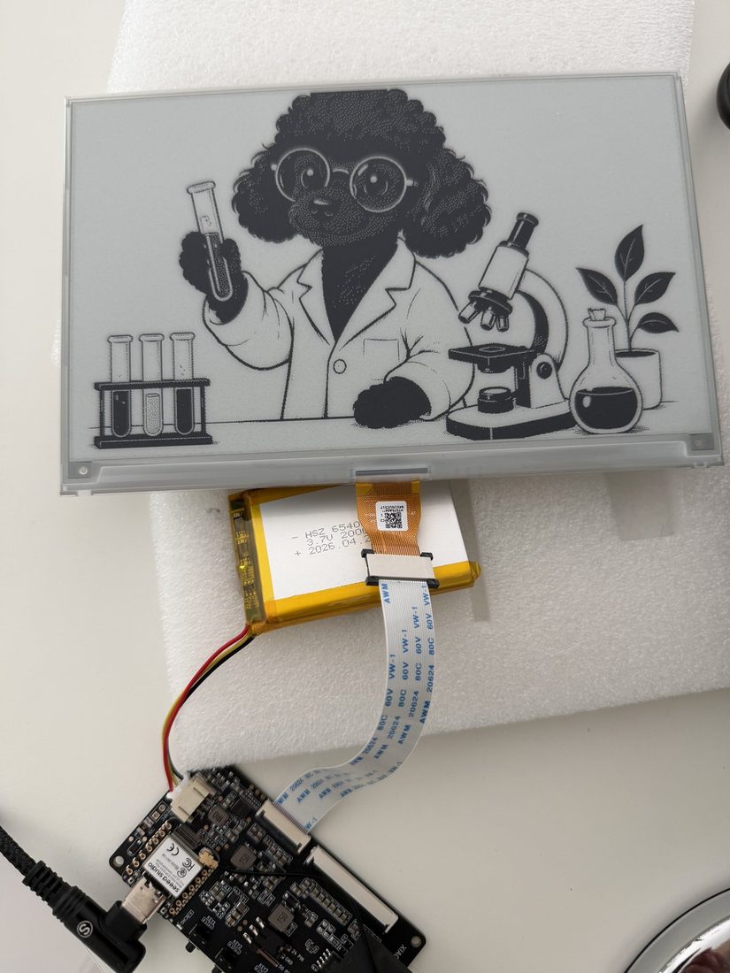 Un pannello a inchiostro elettronico, una scheda ESP32 e una batteria, prima del montaggio.